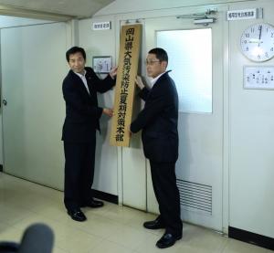 副知事が大気汚染防止夏期対策本部の看板かけをしている写真