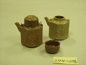 愛知県の瀬戸で焼かれた汽車土瓶。湯呑みを兼ねた蓋がつく。手前の面に「鉄道局指定　お茶」の文字、反対側には「空壜は腰掛けの下へ置くかお持ち帰りください」との注意書きがある。